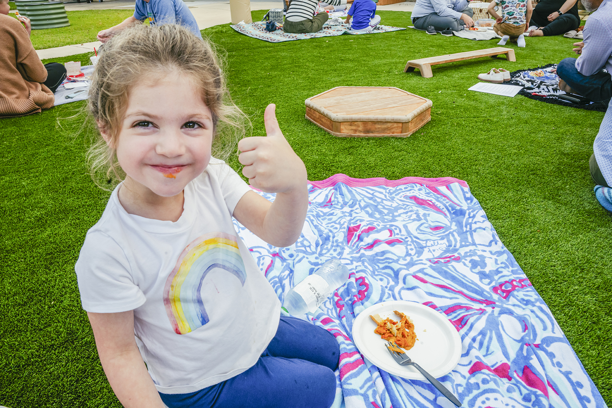 Girl sitting in grass gives a thumbs up after tasting a sweet potato