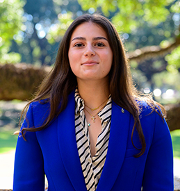 Cristina Hethmon wears a striped blouse and cobalt blue blazer in this headshot taken underneath a beautiful oak tree.
