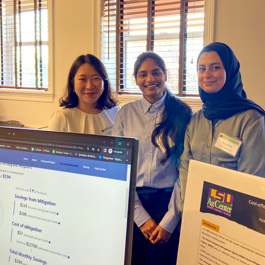 three researchers smile behind a board and a computer screen that present their work