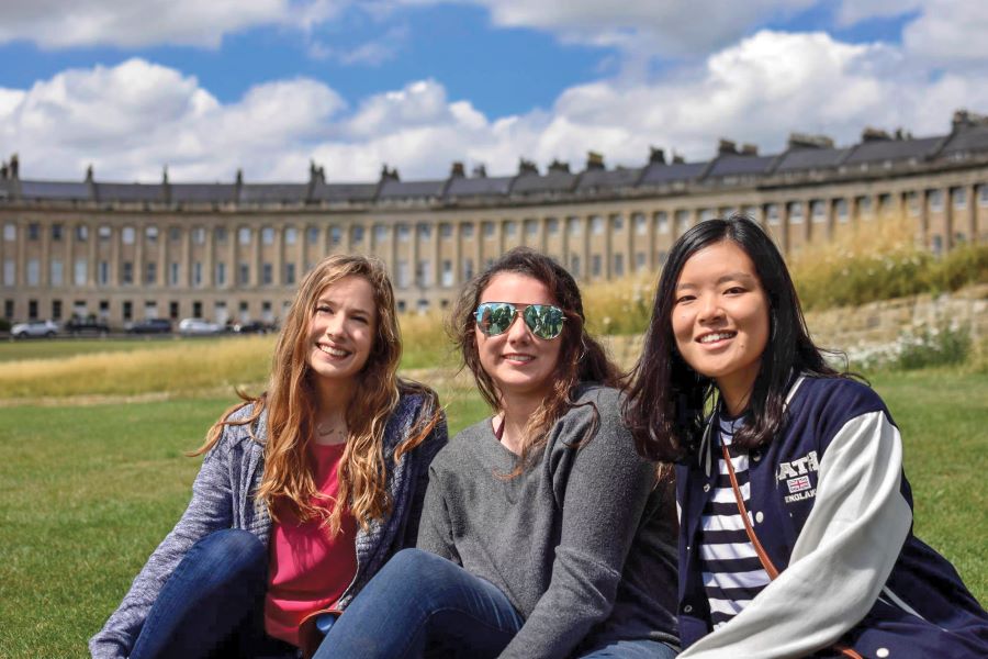 three students smile in front of an ancient building